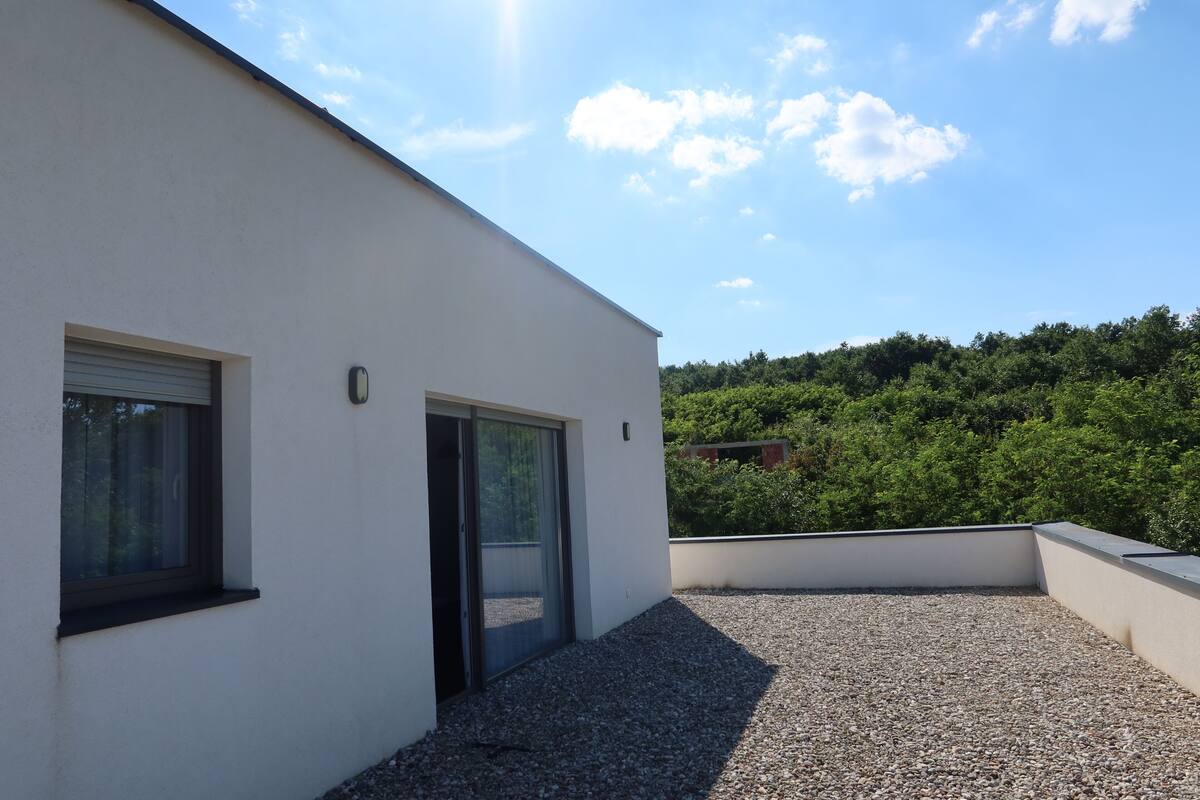 Un bâtiment moderne doté d’un toit plat, d’une terrasse en gravier et d’une porte donnant sur un espace abrité.