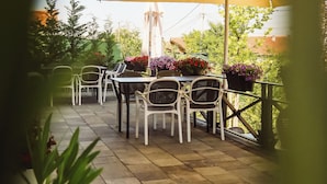 An outdoor patio with tables and chairs under a large umbrella, surrounded by potted plants and greenery. - Andoena Resort (Lipjan)