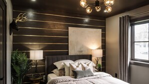 Une chambre à coucher moderne avec un grand lit, des lampes de chevet, un luminaire au plafond et une fenêtre avec des rideaux.