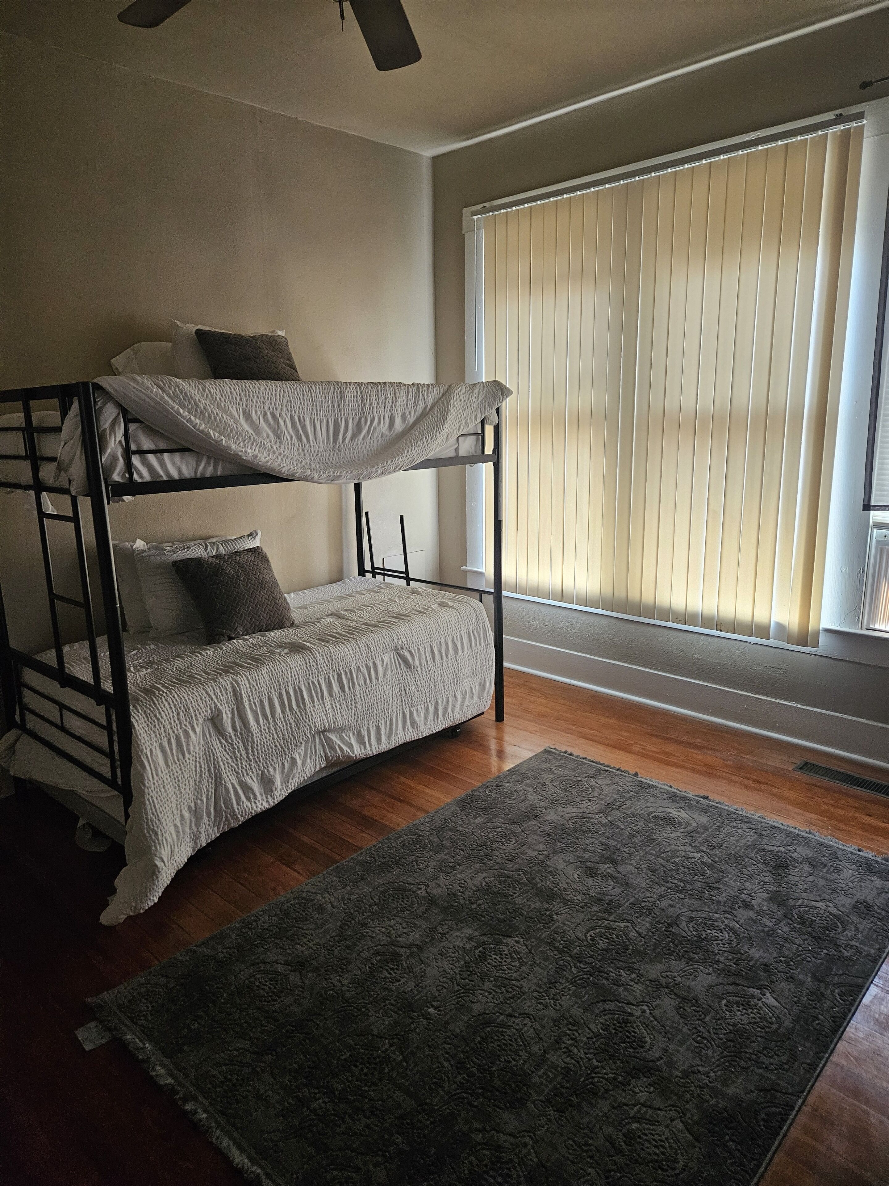 A bunk bed with a grey blanket, a grey rug, and a window with blinds.