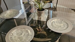 A glass-top dining table with four ornate silver plates, a potted plant, and two glass mugs. - Central! Minutes to Magnolia, Baylor University, Cameron Park  Zoo and more.  (Waco)