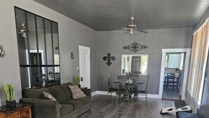 A spacious living room with a gray couch, a dining area with a table and chairs, and a ceiling fan. - Central! Minutes to Magnolia, Baylor University, Cameron Park  Zoo and more.  (Waco)