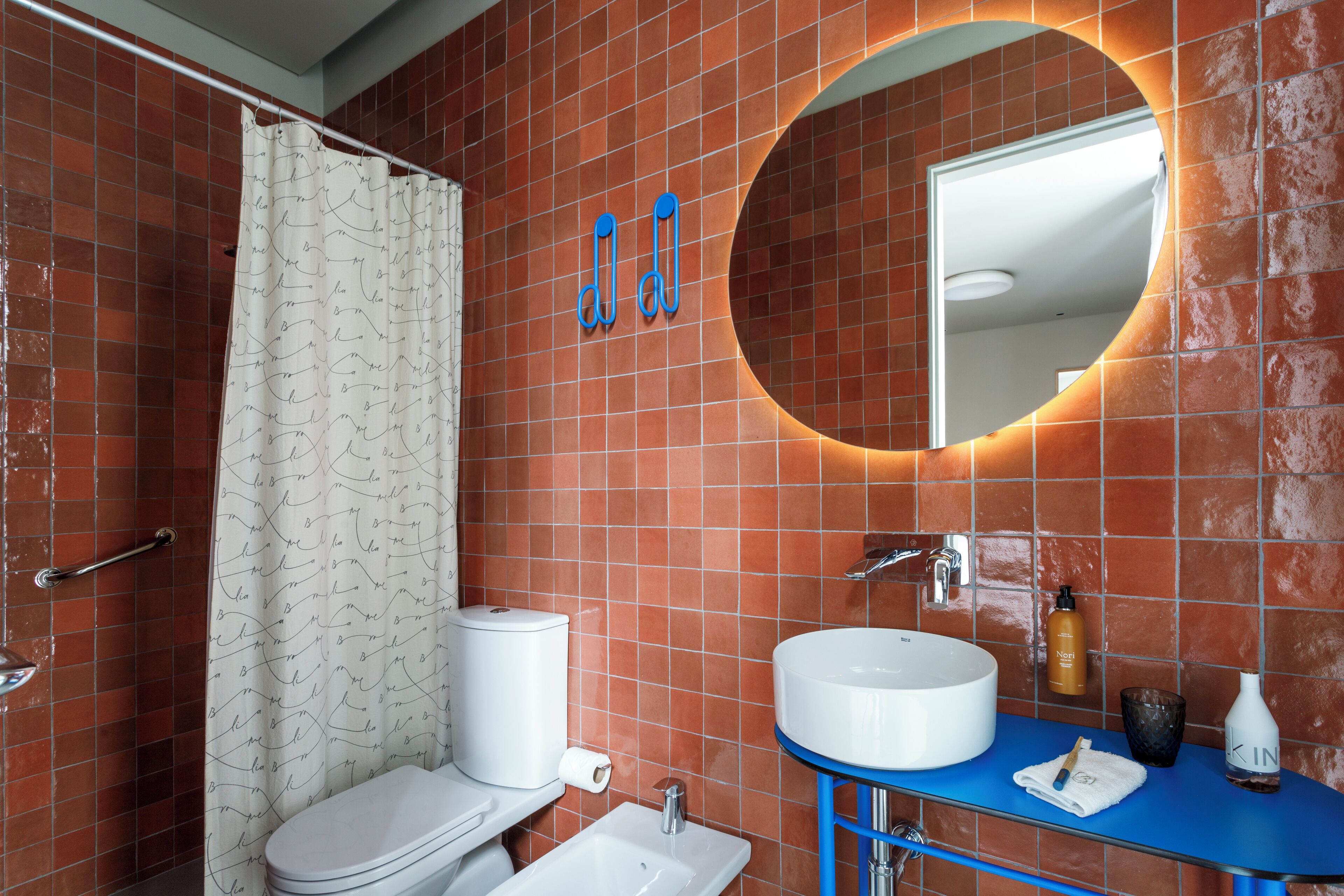 Un baño con inodoro blanco, lavabo con encimera azul y espejo de marco circular.