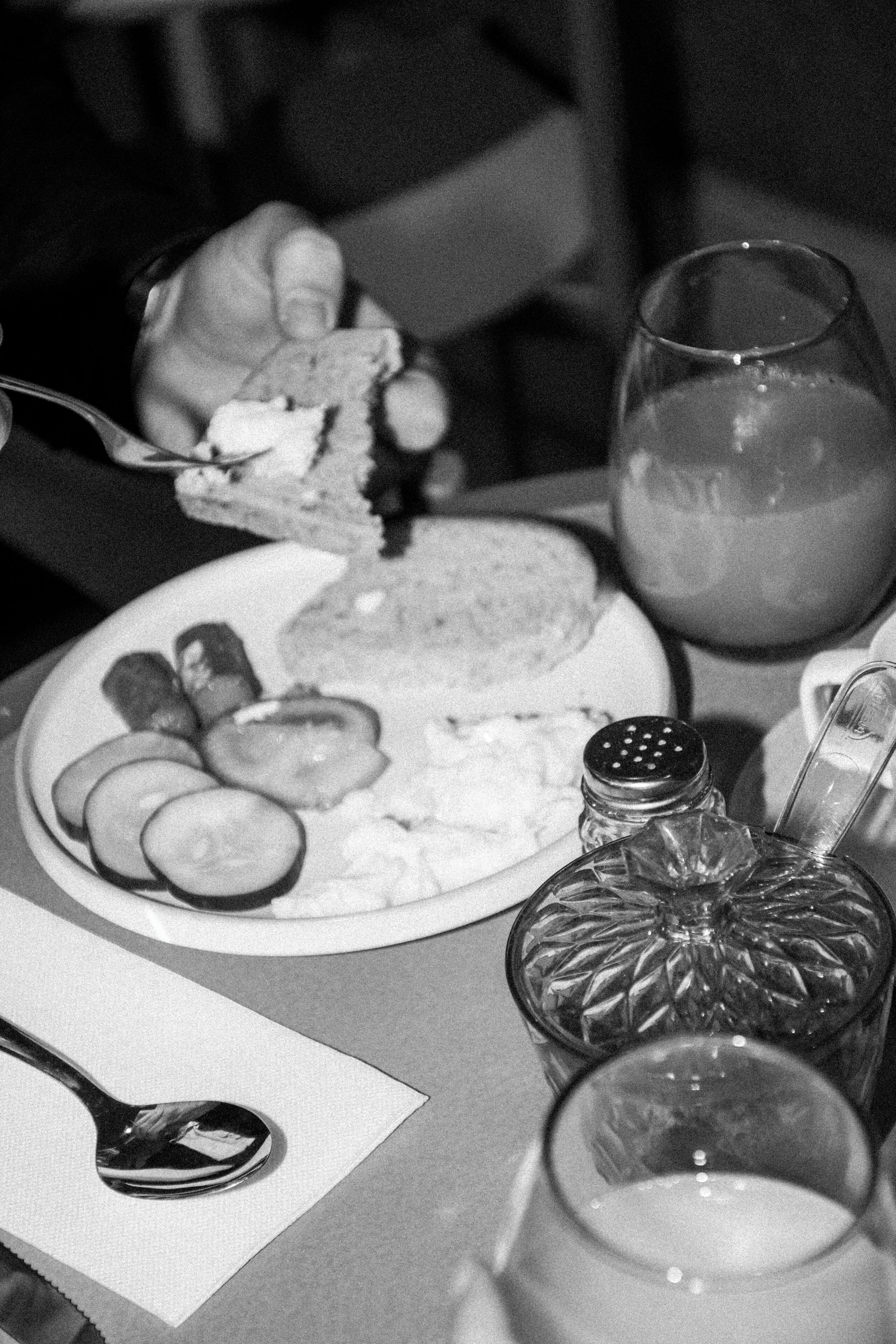 A dining table with a plate of food, a glass of water, and a salt shaker.