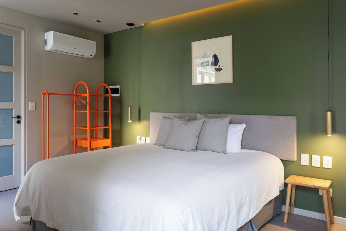 Une chambre à coucher avec un grand lit, un banc en bois, une échelle et un climatiseur fixé au mur.