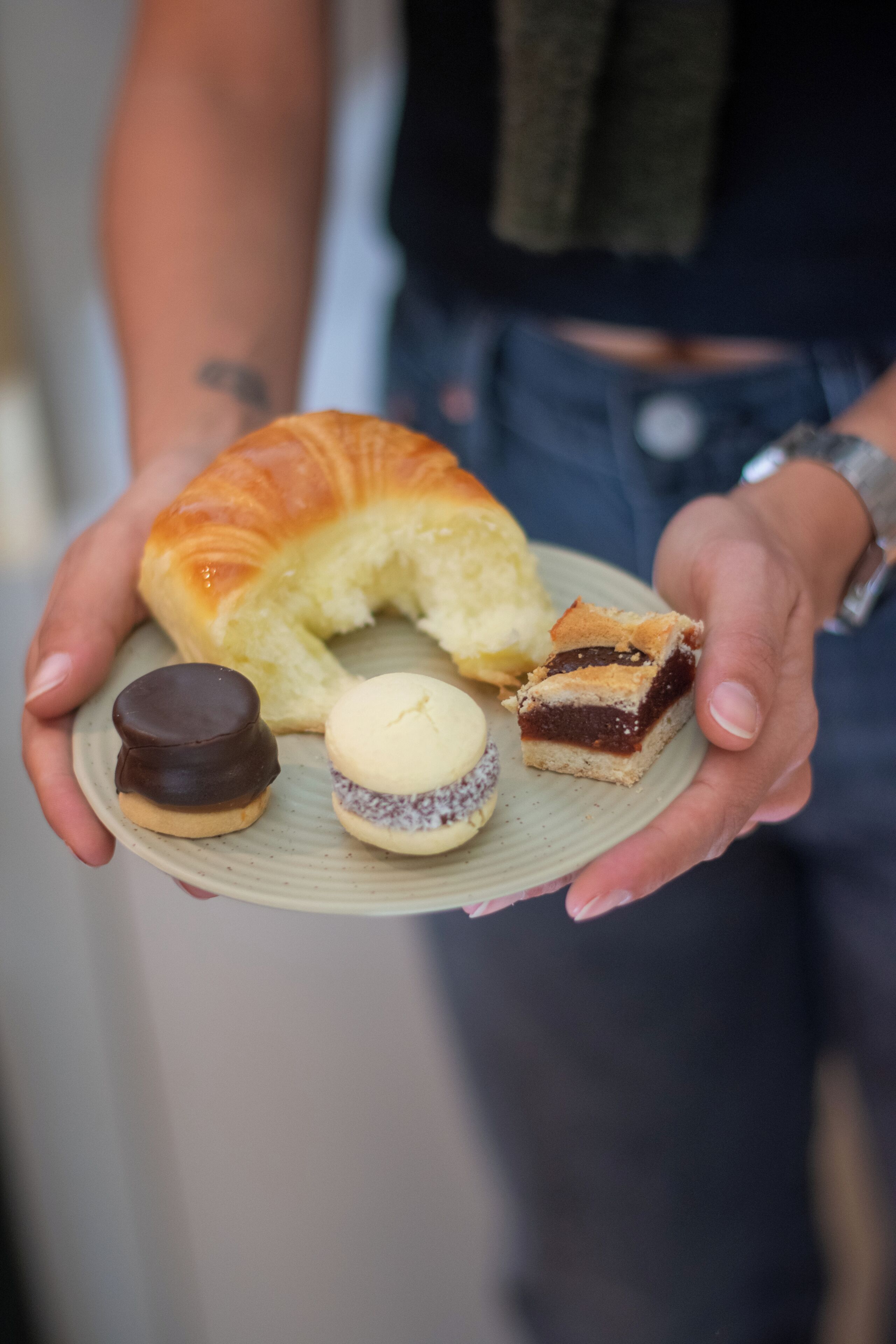 Una persona sosteniendo un plato con un croissant, una galleta con chocolate y un sándwich.