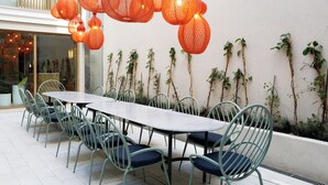 Een eethoek met een lange tafel en stoelen, hangende lantaarns en klimplanten tegen een muur.