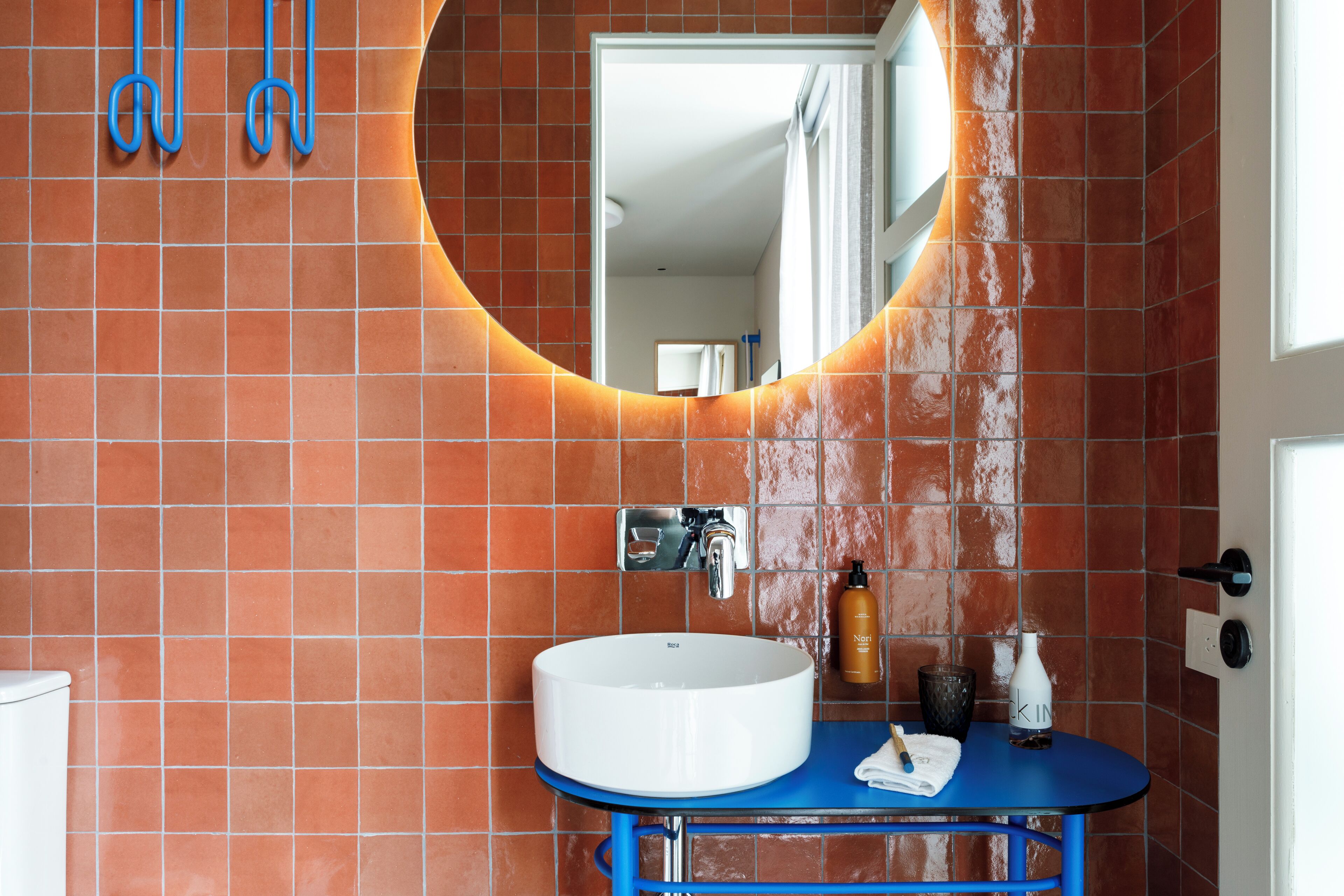 Un baño con lavamanos blanco, encimera azul y paredes con azulejos naranjas.