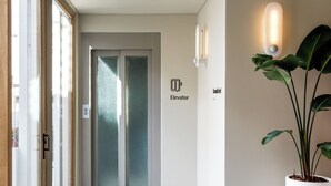 Een moderne lift met een deur van gefroste glas, een wandlamp en een potplant.