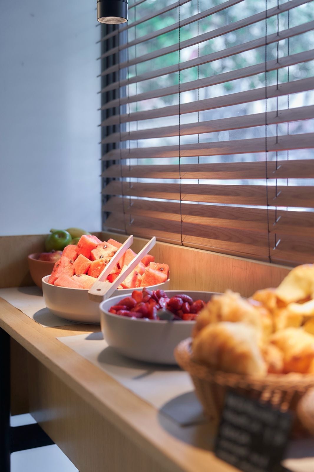 A breakfast buffet with bowls of fruit and pastries, a bowl of apples, and a basket of bread.