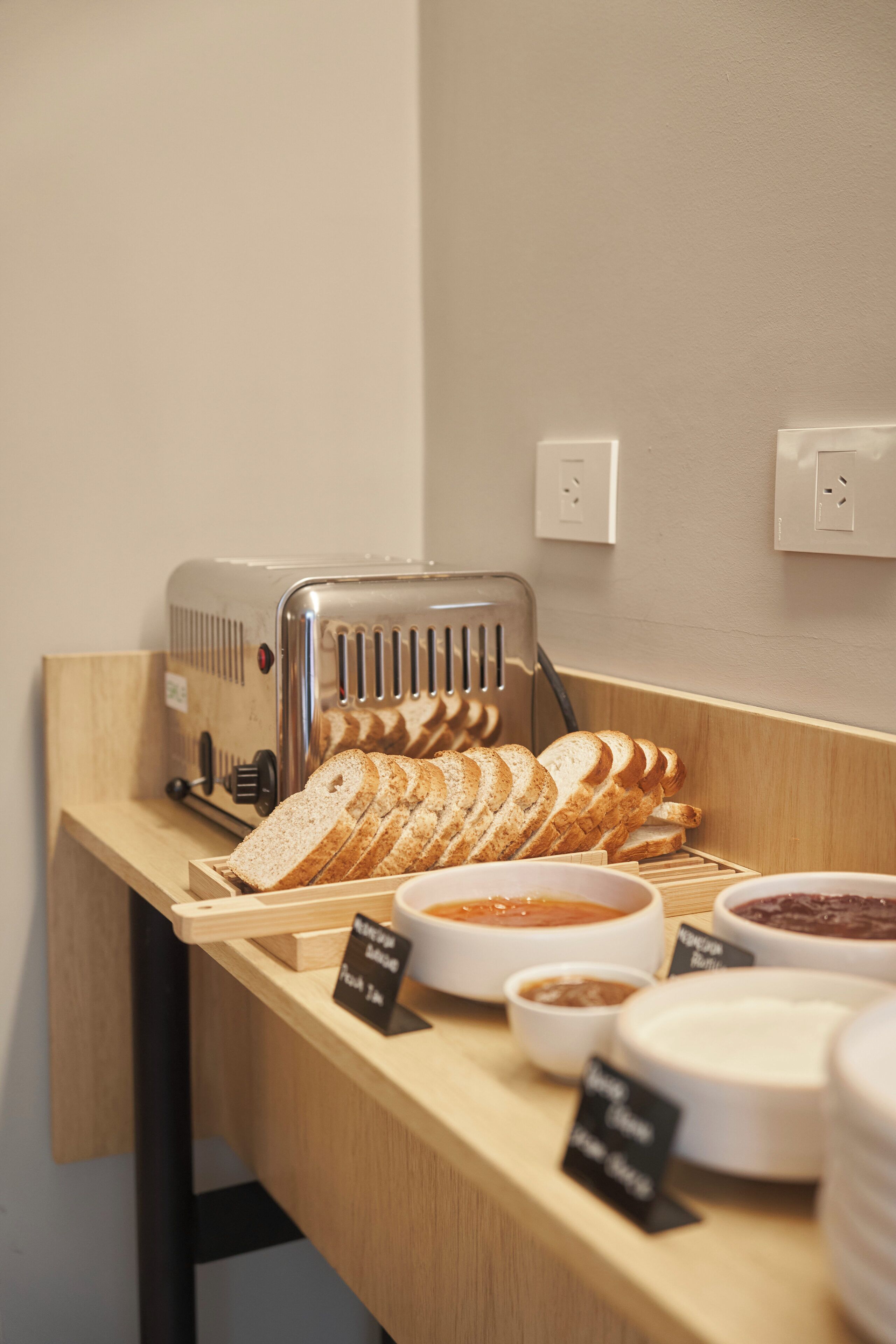 Un buffet della colazione con pane a fette, marmellate e un tostapane.