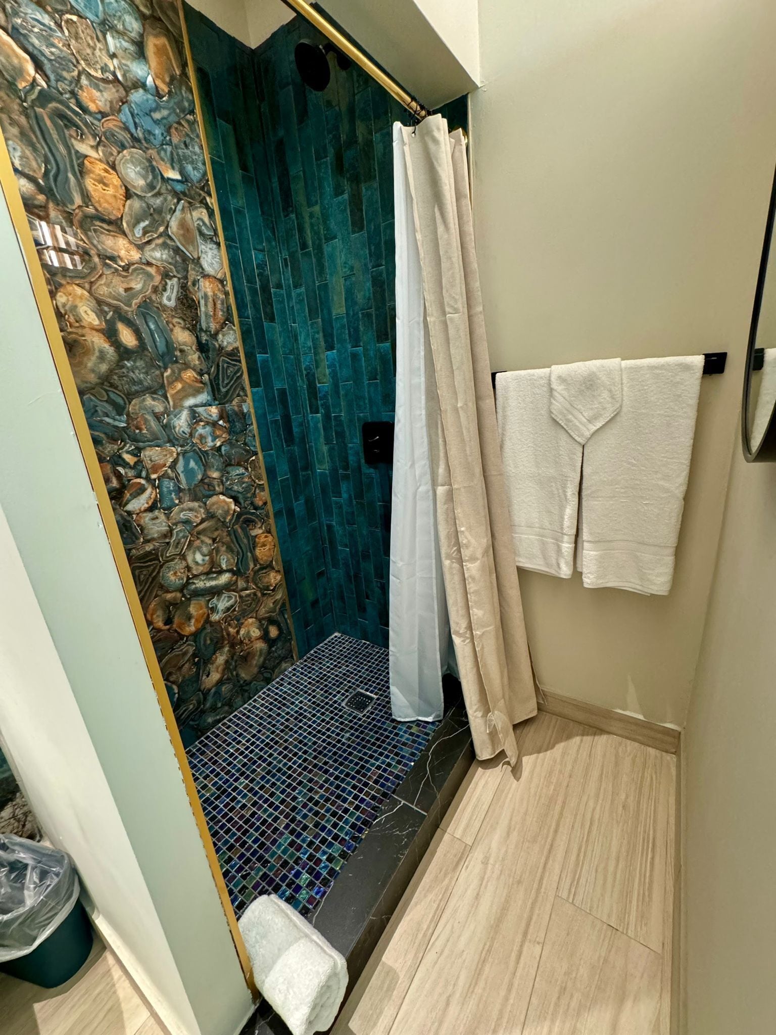 A bathroom with a stone wall, a shower with a tiled floor, and a towel rack with two towels.