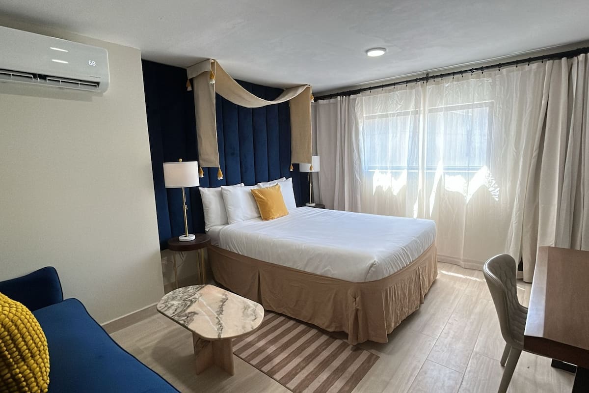 Een hotelkamer met een bed, een kleine tafel, een stoel, een bank en een raam met gordijnen.