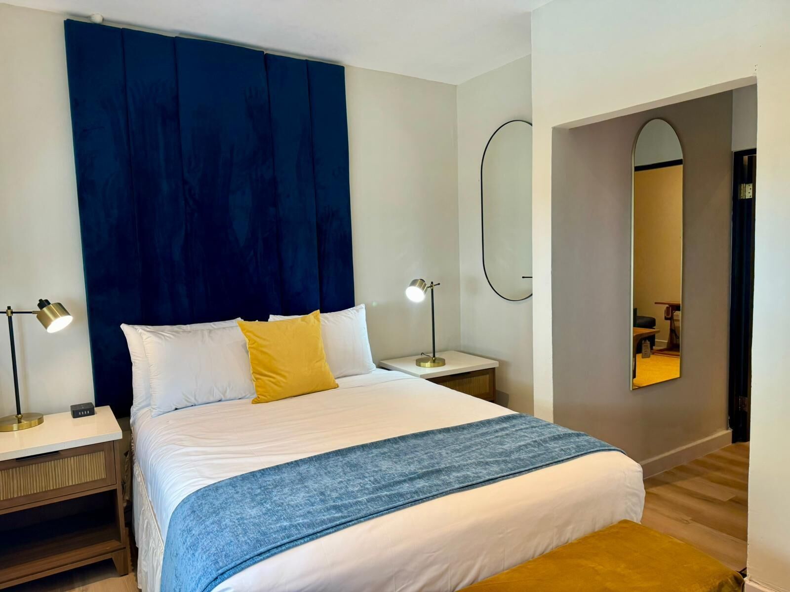 A modern bedroom with a large bed, a bedside table, a nightstand, a mirror, and a blue headboard.