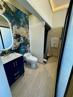 Une salle de bain moderne avec un mur en marbre, des toilettes blanches, un meuble-lavabo bleu foncé et un espace douche.