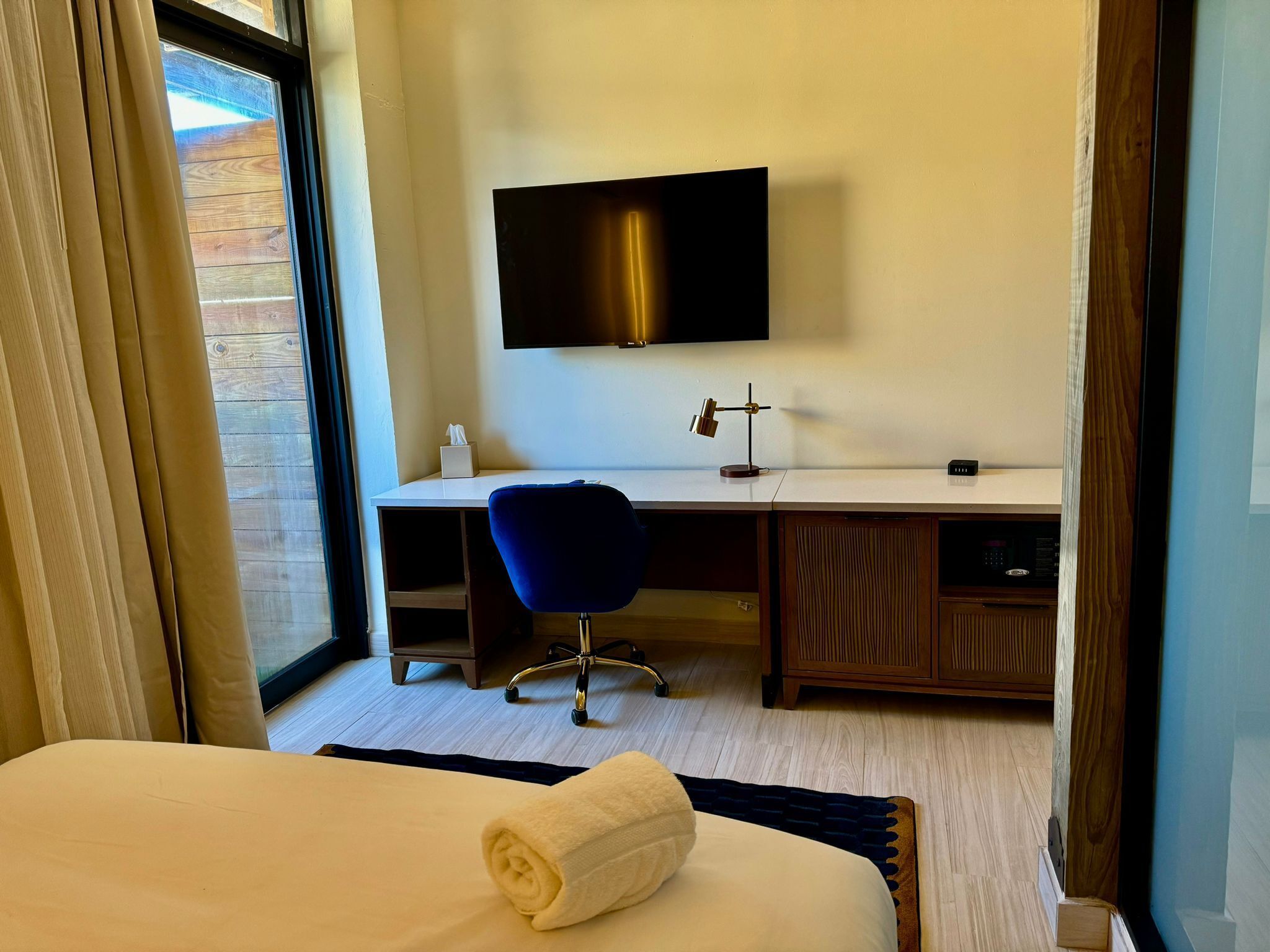 Une chambre d’hôtel équipée d’un lit, d’un bureau, d’une chaise, d’une télévision et d’une fenêtre avec des rideaux.