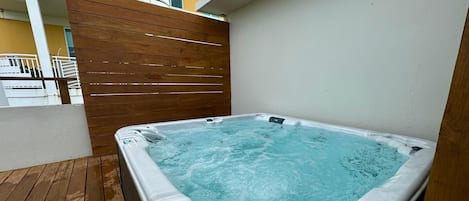 A hot tub on a wooden deck with a view of a building in the background.