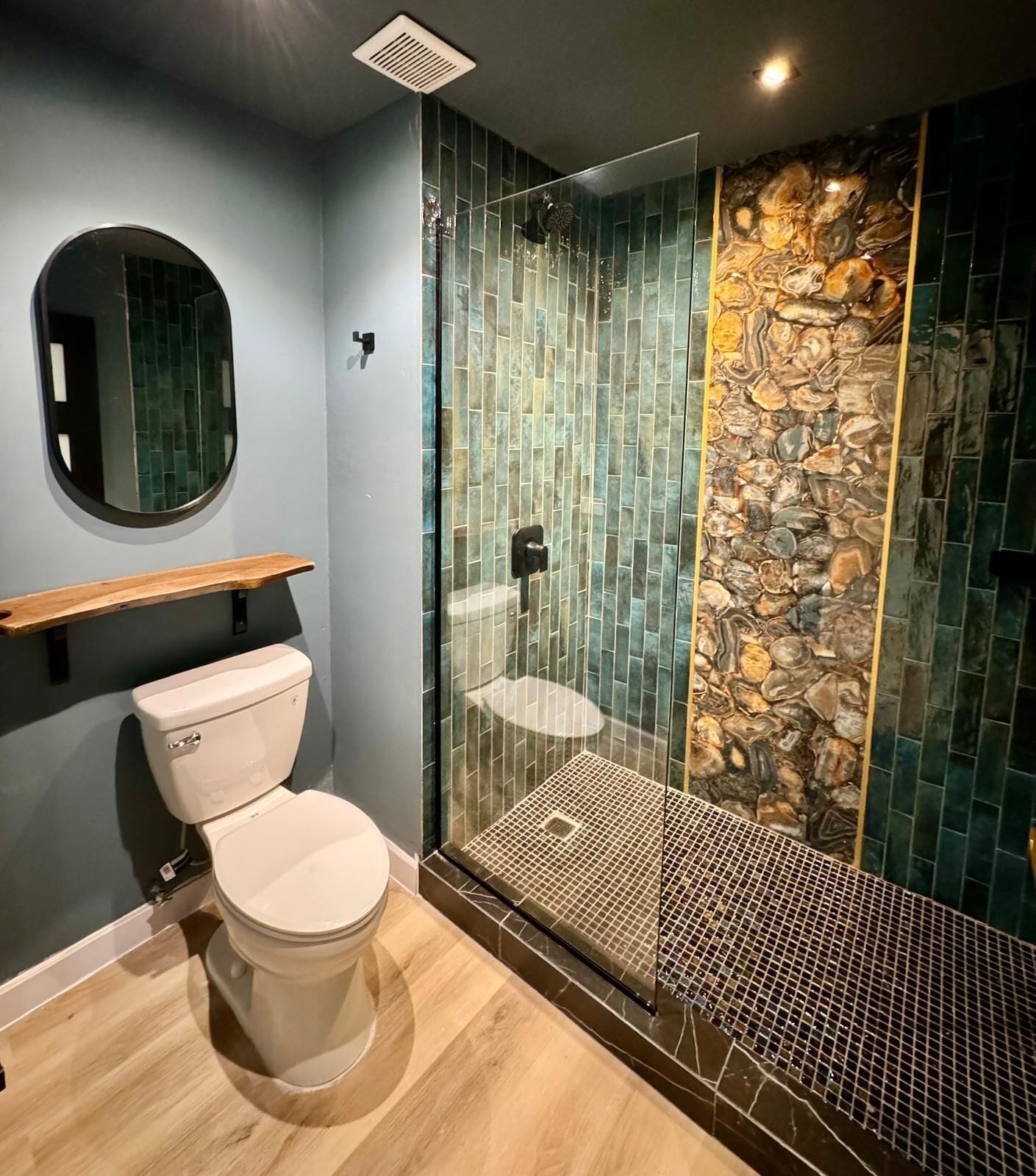 Un baño moderno con inodoro, ducha con puerta de vidrio y pared de piedra.