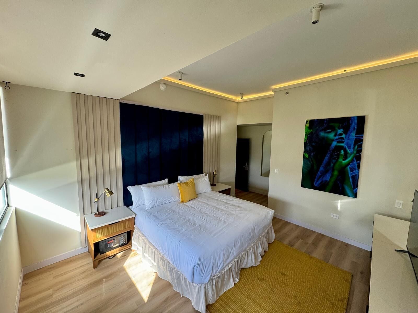 Een moderne slaapkamer met een groot bed, nachtkastje, spiegel en wanddecoratie.