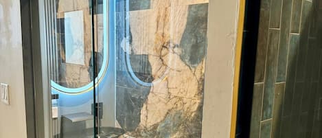Un baño moderno con ducha envuelta en vidrio, paredes de mármol y un inodoro.