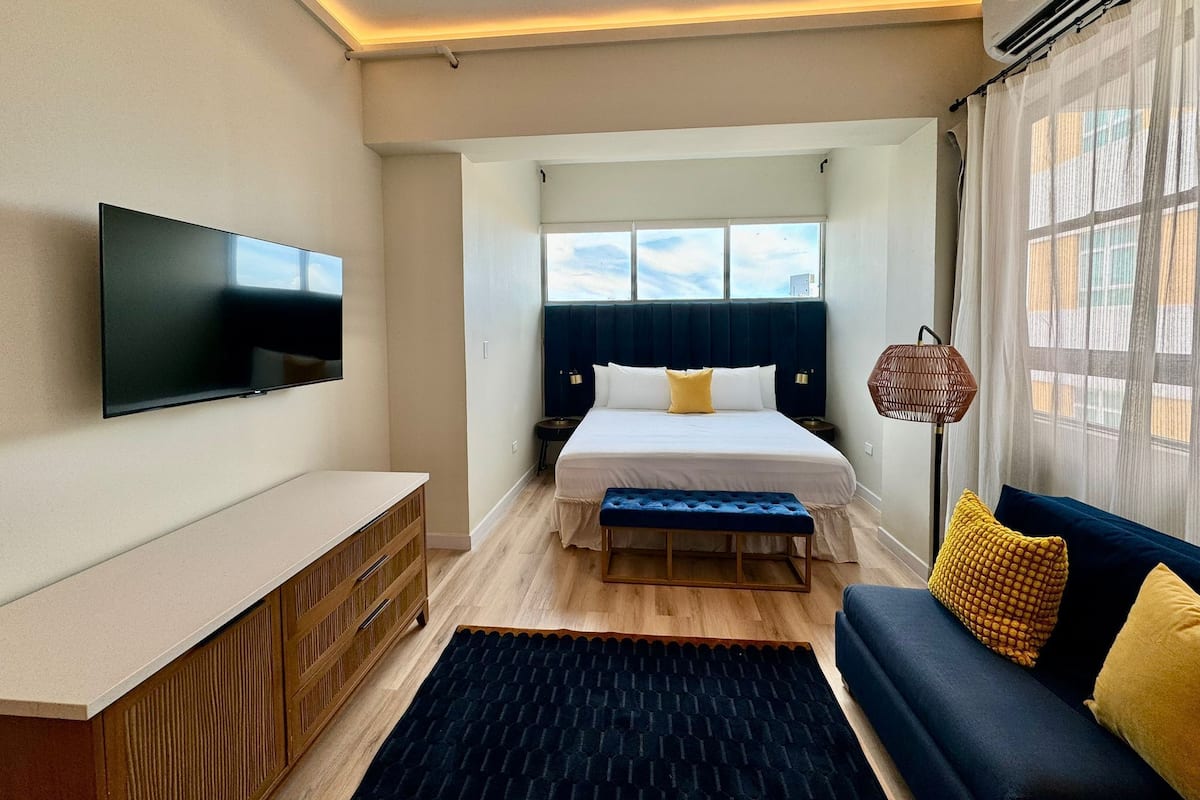 Een moderne hotelkamer met een flatscreen televisie, een bed met hoofdeinde, een sofa, een klein tafeltje en een raam met gordijnen.