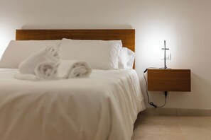 A neatly made bed with white linens and pillows, a wooden headboard, and a bedside table with a lamp and power outlet. - Suite - Pumo by MONHOLIDAY (Monopoli)