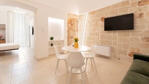 A modern living room with a stone wall, a flat-screen TV, a round dining table with chairs, and a green sofa.