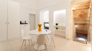 A modern kitchen with white cabinets, a dining area with a round table and chairs, and a staircase with a stone wall.
