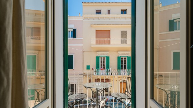 A balcony with a table and chairs, a view of buildings with balconies, and a clear sky.
