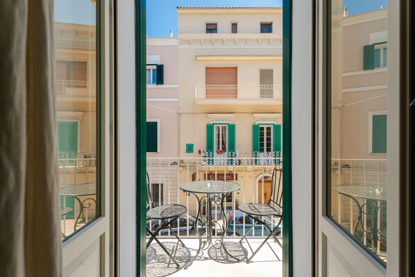 A balcony with a table and chairs, a view of buildings with balconies, and a clear sky.
