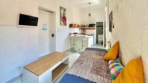 A compact living space with a kitchenette, a dining area with a bench, and a sofa with cushions.