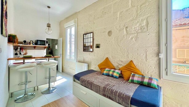 A compact bedroom with a bed, a small kitchenette, and a window.