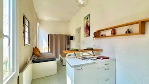 A compact living space with a bed, a dining table, a kitchen area, and a small seating area.
