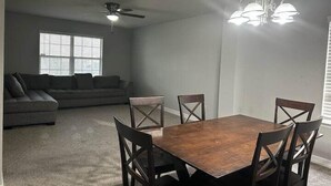 A dining area with a wooden table and chairs, a ceiling fan, and a window with blinds. - Cute And Cozy Hostel (Houston)