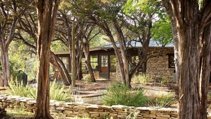 Un edificio de piedra con puerta y ventanas de vidrio, rodeado de árboles y un muro de piedra.