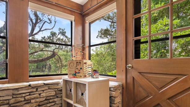 Una habitación con pared de piedra, puerta de madera y ventanas amplias con vista a árboles.