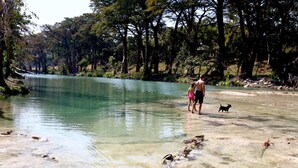 Un río cristalino con gente y un perro cerca de la orilla, rodeado de árboles.