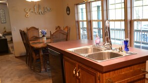 Una cocina con armarios de madera, un lavamanos doble y una zona de comedor con sillas y una mesa.
