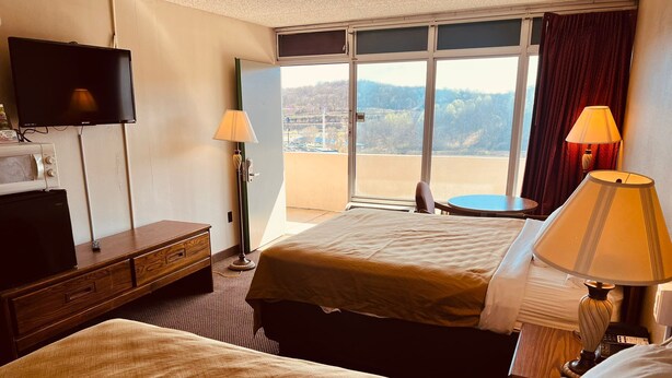 A hotel room with two beds, a TV, a desk with a lamp, and a view of the outdoors.