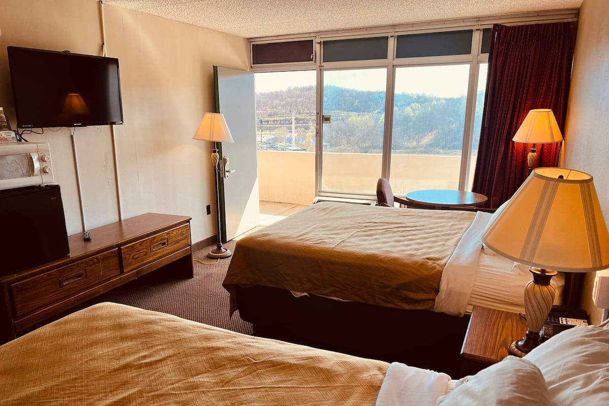Habitació d'hotel amb dos llits, una televisió, escriptori amb làmpada i vista a l'exterior.