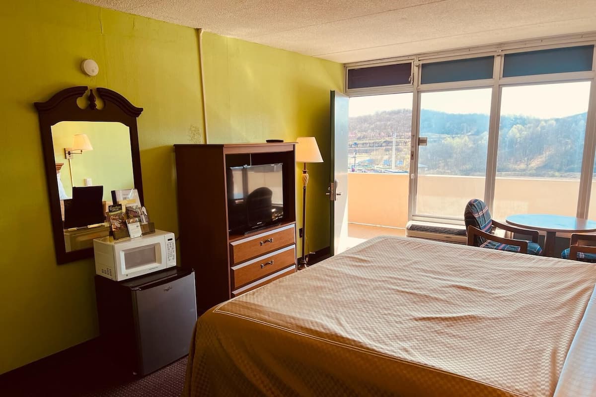 Una habitació d'hotel amb un llit, una televisió, un microones, una petita taula de nit i un balcó amb vista a les muntanyes.