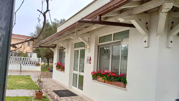 A building with a stone pathway leading to a door, potted plants on the windowsills, and a white fence in the background. - Il Focolare  (Fiumicino)