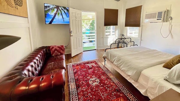 A bedroom with a bed, a red sofa, a ceiling fan, a TV, and a window with blinds. - Comfy Hideaway: Walk to Restaurants and Nightlife (Houston)