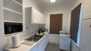 A compact kitchen with white cabinetry, a microwave, a stove, and a sink. - Comfy Hideaway: Walk to Restaurants and Nightlife (Houston)
