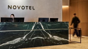 Een receptiebalie met een marmeren blad en de naam 'NOVOTEL' op de achtergrondmuur.