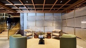 Een moderne lobby met een trap, twee fauteuils, een bijzettafeltje en een decoratieve vaas.