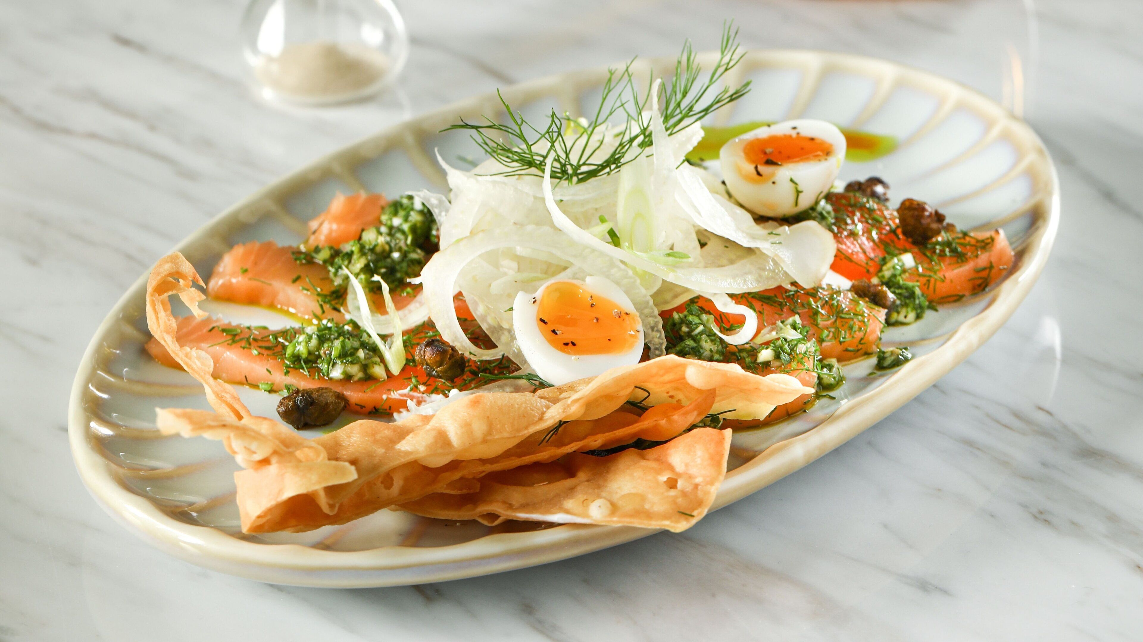 Un plato de comida con salmón, huevos y verduras sobre una mesa de mármol.