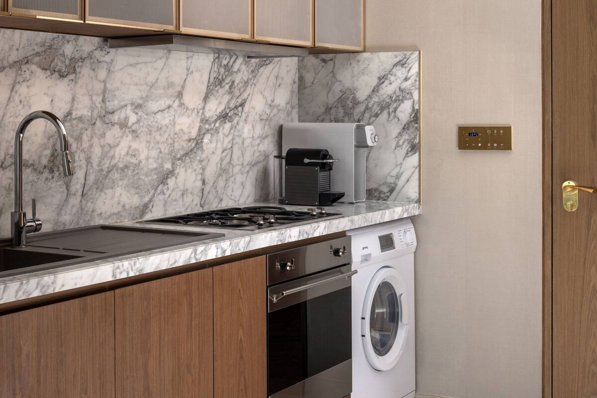 Een kleine keuken met een marmeren aanrecht, roestvrijstalen apparatuur en houten keukenkastjes.