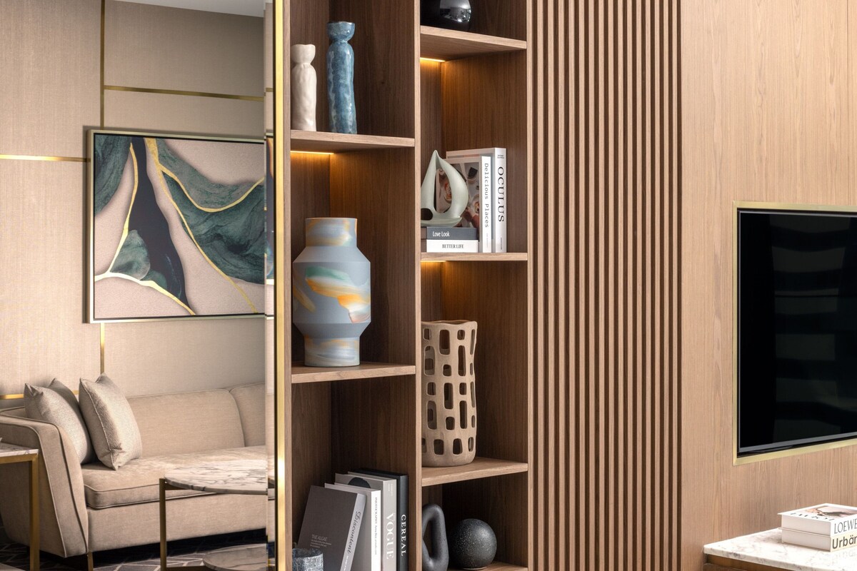 Un salon moderne comprenant un canapé, une table basse, une table d’appoint avec une lampe, une bibliothèque agrémentée d’objets décoratifs et un grand tableau abstrait.