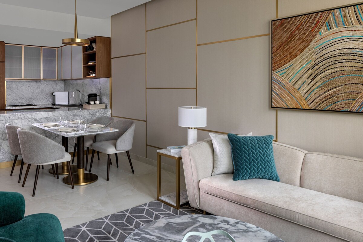 Un salon moderne comprenant un canapé, une table à manger pour quatre personnes et un coin cuisine avec des meubles en bois et un plan de travail en marbre.